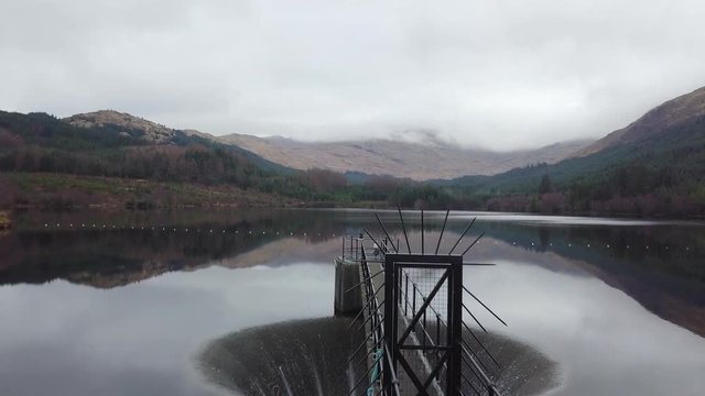Aerial reveal of the incredible Gleann Dubh Reservoir surrounded by cloud shrouded mountains and forrest in Scotland, UK