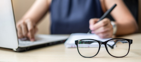 Close up eye glasses with Businesswoman using laptop analysis marketing plan background. Business, Finance and Vision concepts