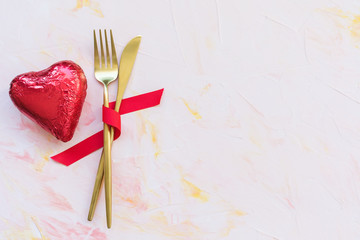 Golden cutlery in red ribbon and heart on a pink background