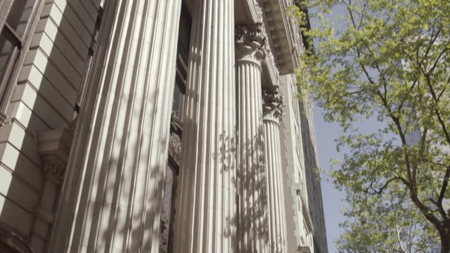 Wide tilting shot of a White building with pillars lit by sun through trees in Portland, Oregon, USA