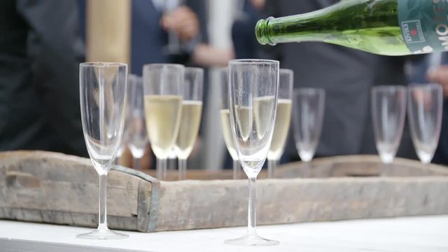 Swedish apple cider pouring in slow motion from a bottle into champagne glasses. Blurred background with people at an event in the background.