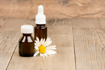 camomile flowers and essential oil in brown glass bottles on wooden rustic table