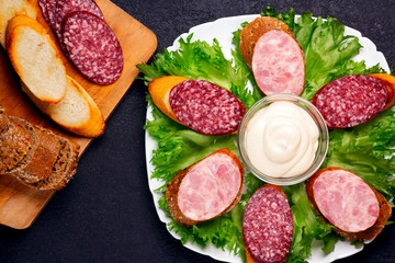 Several sandwiches with sausage and salami and sauce on a plate, flat lay