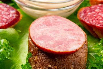 Several sandwiches with sausage and salami and sauce on a plate, close up