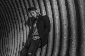 Muscular young man with beard on dark tunnel urban background. Fashion portrait of brutal strong muscle guy with modern trendy hairstyle. Model, fashion concept. Sexy naked torso. Black and white.