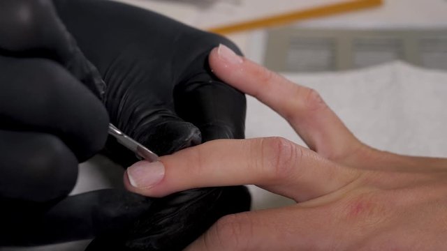 Close up macro finger nail care by manicure specialist in beauty salon. Manicurist clear cuticle professional scissors for manicure and pedicure.