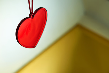 A red glass heart with a golden and white blurred background. Love and Valentine concept. Copy space.