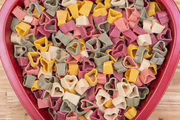 Background made of durum wheat semolina heart-shaped 5 flavors pasta with vegetables. Valentine's Day. 