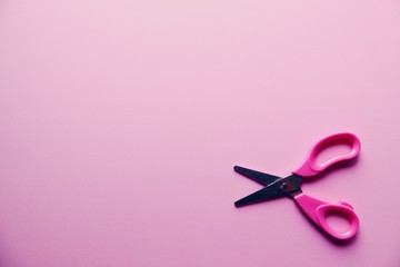 Small pink scissors on pink background close up