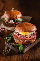 Homemade beef burger with crispy bacon and vegetables on rustic serving board