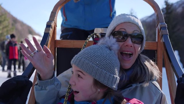 A cute young girl and her mother dogsledding through the snow and waving to their friends on the wilderness trail in slow motion.