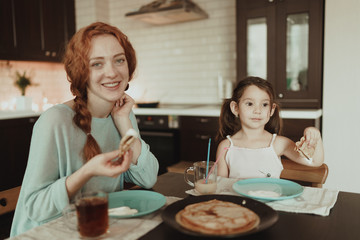 beautiful happy girl and woman eat pancakes in kitchen