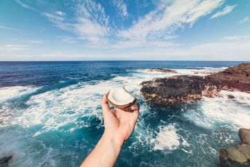 Fototapeta na wymiar Tropical ocean beach vacation relax travel concept. Coconut in hand on ocean rock beach.