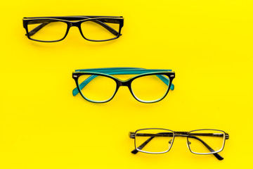 Set of glasses with transparent lenses on yellow background top view copy space