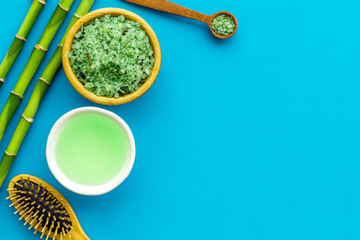 Asian spa treatment concept with natural ingredients. Spa salt, lotion, sponge near bamboo on blue background top view space for text