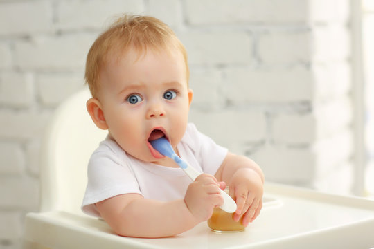 Baby 7 months in a child seat in front of the window eats food from a spoon