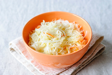 Orange bowl with crunchy sauerkraut served on napkin with forks on table