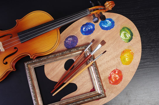 Violin, art palette, brushes, picture frame on a black background