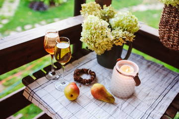 beautiful summer evening on wooden terrace or patio. Table with two glasses of wine, fruits and flowers