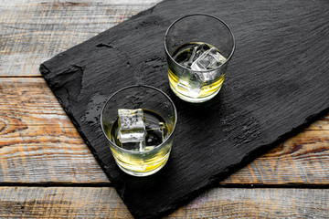 In the bar. Whiskey with ice on black desk on wooden background top view copy space