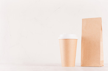 Coffee branding identity mockup in minimalist style - kraft brown paper cup and blank packet closeup, with copy space on white wood board.