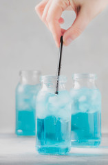 Hand puts straw in drink. Sport and fitness drink concept, cold isotonic blue water in bottles, gray table background, selective focus