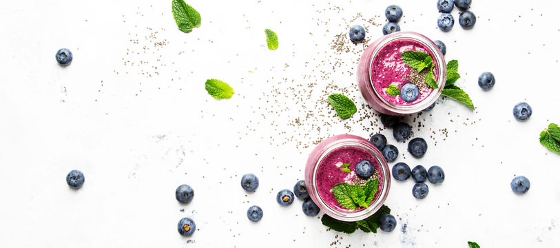 Purple homemade yogurt or smoothie with blueberries, chia seeds and mint leaves in glass jars on white background, flat lay, top view