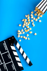 Film watching concept. Clapperboard and popcorn on blue background top view copy space