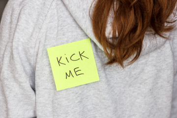 Fool'day jok. Sticker 'Kick me' on teenager girl's back.