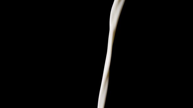Macro shot of pouring milk in slow motion in front of black background.
