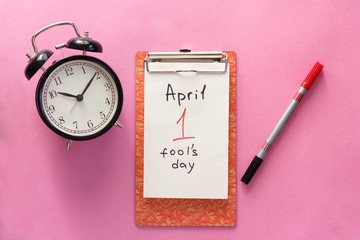 1 april fool's day, notebook, clock, pen. Flat lay on pink background.
