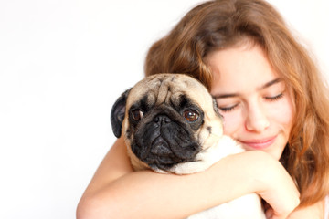 Cute teen girl hugging and kissing a pug dog on white background