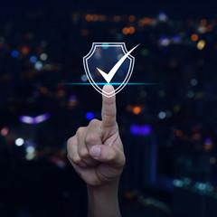 Hand pressing security shield with check mark icon over blur colorful night light city tower and...