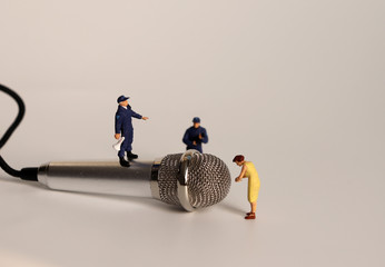 A miniature woman standing in front of a microphone and a miniature policeman standing on a...