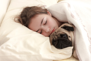 Pretty teen girl sleeps hugging a pug dog in bed