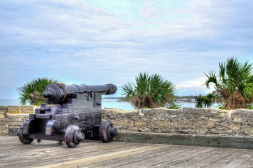 A Spanish colonial cannon on top of an old Spanish fort, overseeing the ocean and palm trees. Shot in Castillo de San Marcos, St Augustine, Florida, USA.