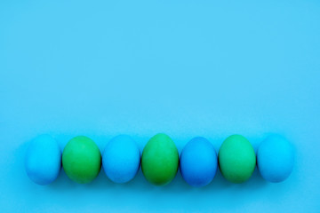The line of dyied on green and blue Easter eggs flatlay on bright blue background. Hand drawn eggs shot as a flatlay.