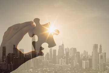 Hand holding puzzle piece against city background 