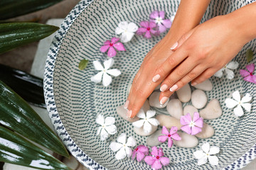Hands of Young girl with natural manicure on fingernails and bowl with water and flower.Spa treatment and massage for female hands.Close up.Spa skin and body nails care concept. Cosmetology.