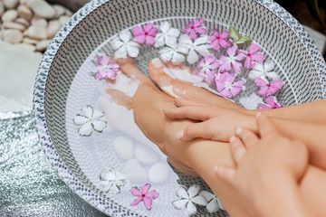 Obraz na płótnie Canvas Spa treatment and product for woman feet and foot spa. Foot bath in bowl with tropical flowers, Thailand. Healthy Concept. Closeup of beautiful female feet, legs at spa salon on pedicure procedure
