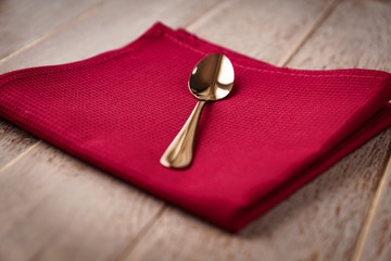 close up of cloth napkin of red color and served tea spoon on wooden table.