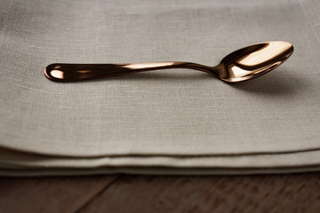 Close up of cloth napkin of beige color and served tea spoon on wooden table.