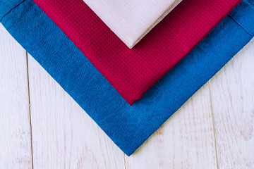 close up of cloth napkins of beige, blue and burgundy colors on rustic white wooden table. Shallow depth of field.