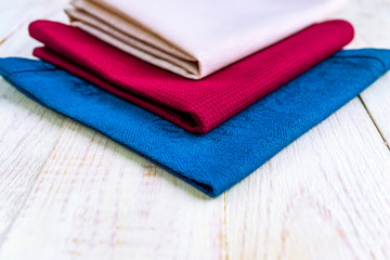 close up of cloth napkins of beige, blue and burgundy colors on rustic white wooden table. Shallow depth of field.