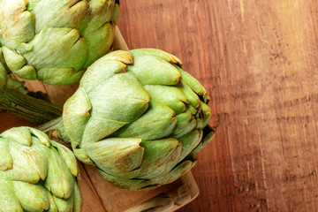 A closeup photo of a globe artichoke on a dark rustic wooden background with a place for text