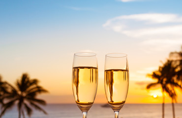 Pair of champagne glasses on tropical sunset background. Romantic beach getaway for two setting.