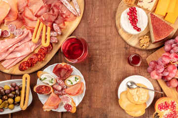 Charcuterie Tasting. A photo of many different hams, lunch meats, and a cheese platter, shot from above on a rustic background with a glass of red wine and a place for text