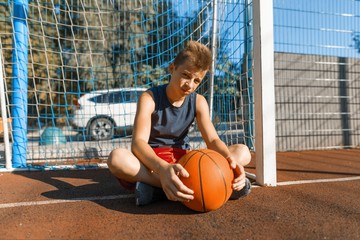 Caucasian teenager boy street basketball player with ball on outdoor city basketball court