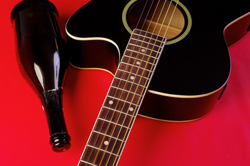 Acoustic guitar and bottle on red.