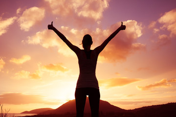 Fototapeta premium Winning, success , and life goals concept. Young woman silhouette with arms in the air putting thumbs up